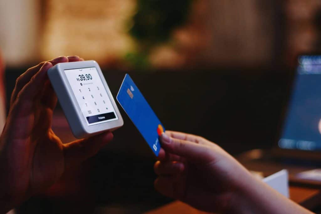 A person holds a small card reader displaying a transaction amount, while another hand holds a blue credit card near the reader, preparing for a contactless payment—ideal for streamlining payments in any rental business.